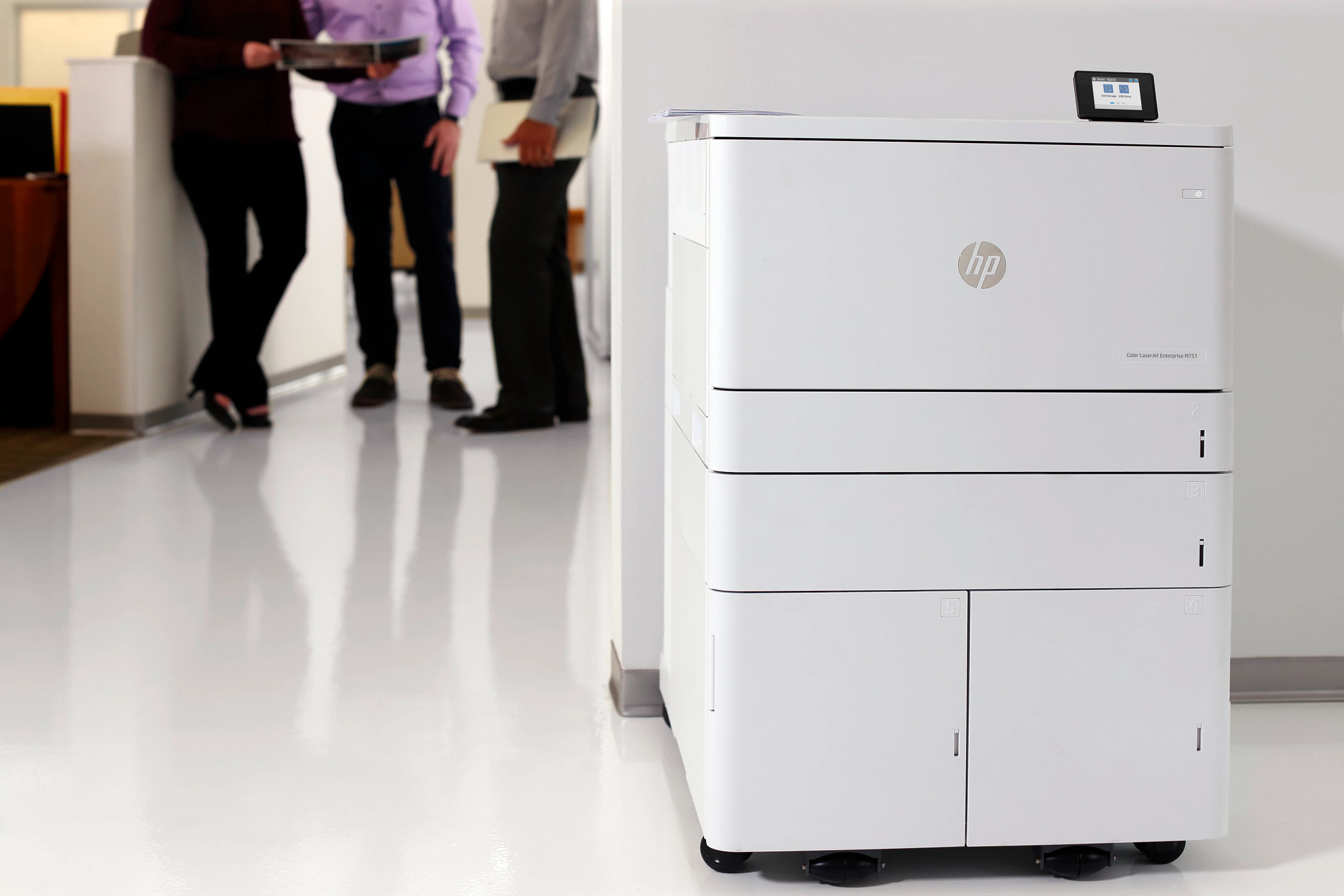 HP A3 Color Printer in the foreground of an office hallway meeting